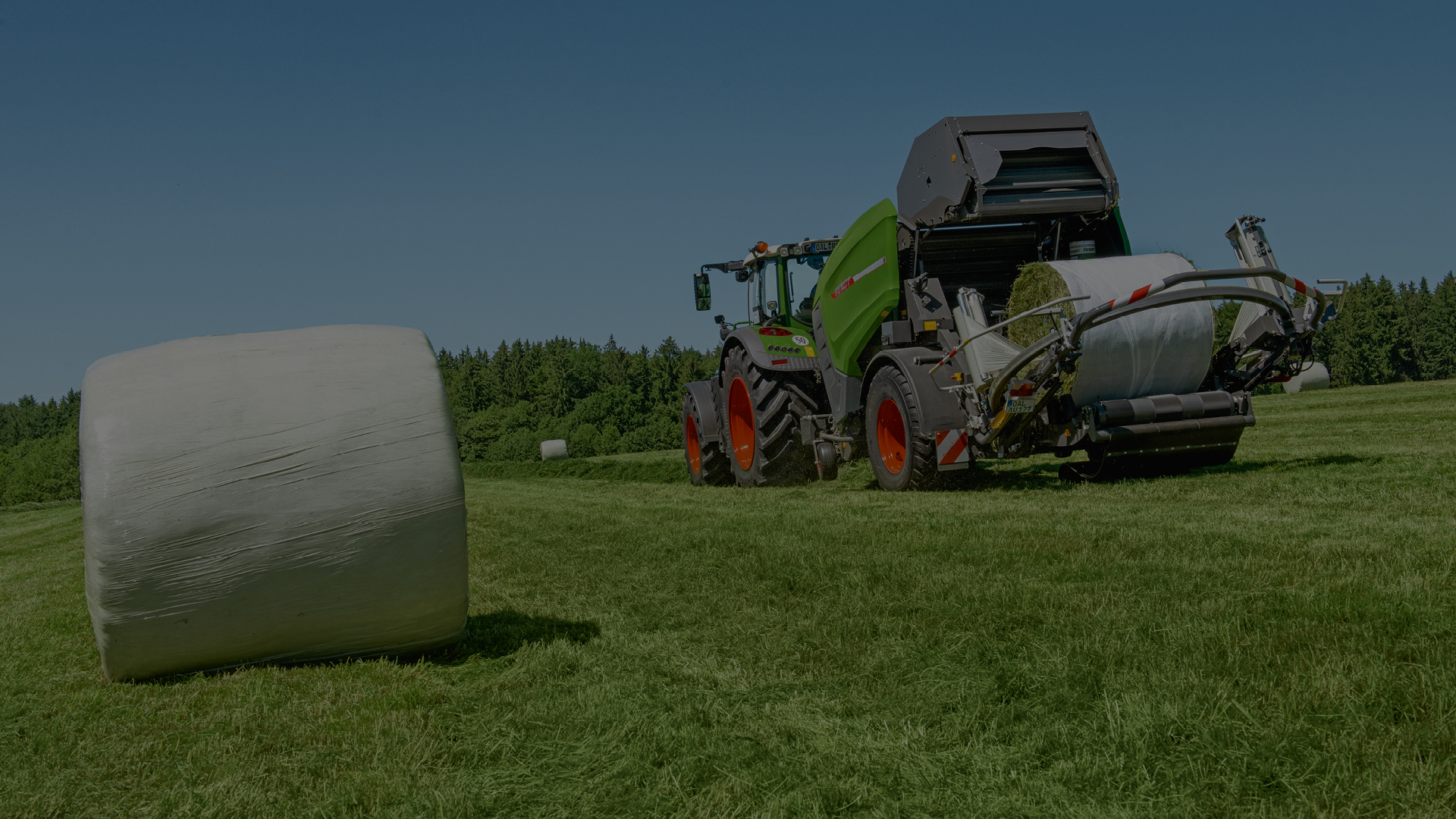 A picture of a Fendt baler on a field with a wrapped bale of hay