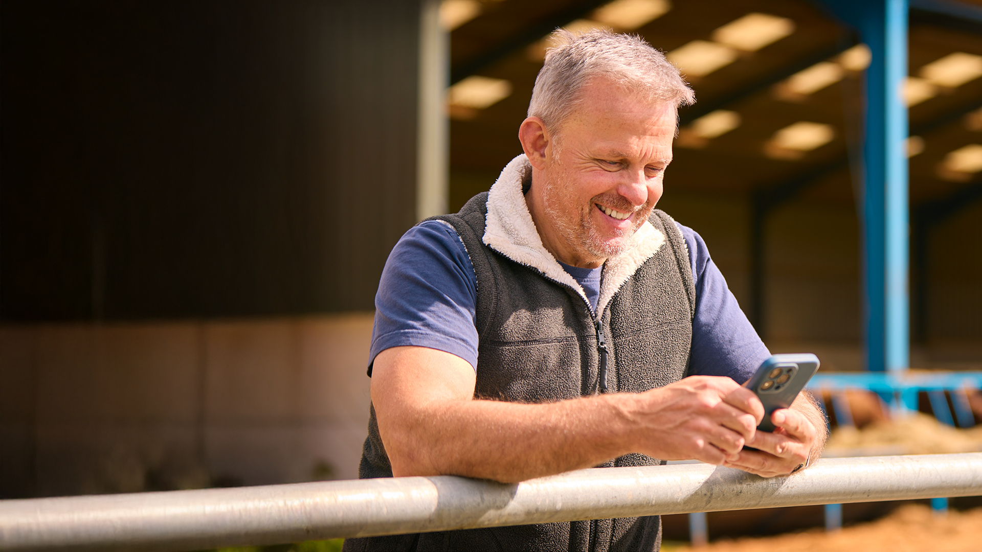 A farmer looking at his phone while standing in a barn and smiling